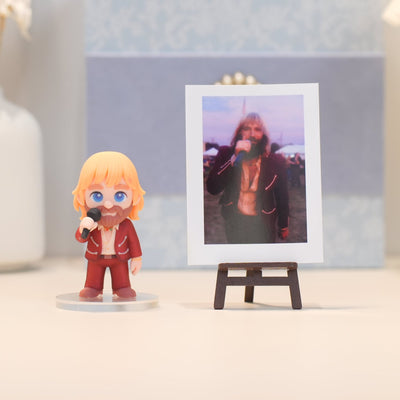 Figurine of a person with blonde hair and a beard holding a microphone next to a framed photo on a stand.