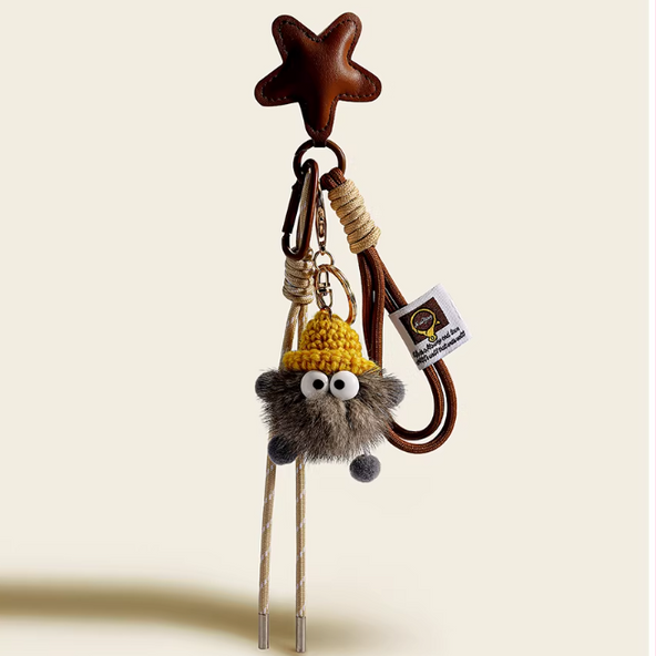 Keychain with a star-shaped hook, bell, and plush character on a beige background
