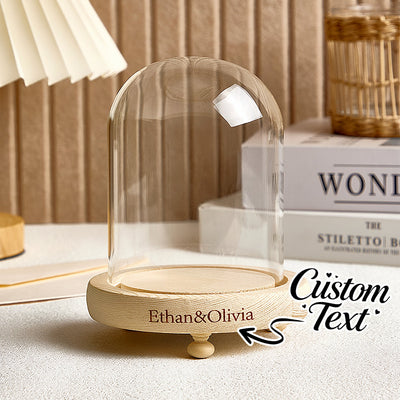 Decorative glass dome with wooden base on a surface, featuring personalized text.