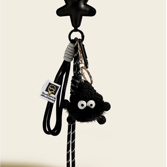 Black plush keychain with googly eyes attached to a strap on a beige background